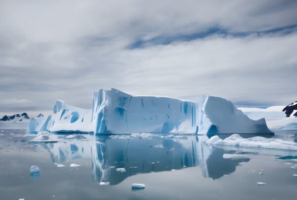 A serene scene of a massive iceberg reflecting in still waters against an overcast sky.