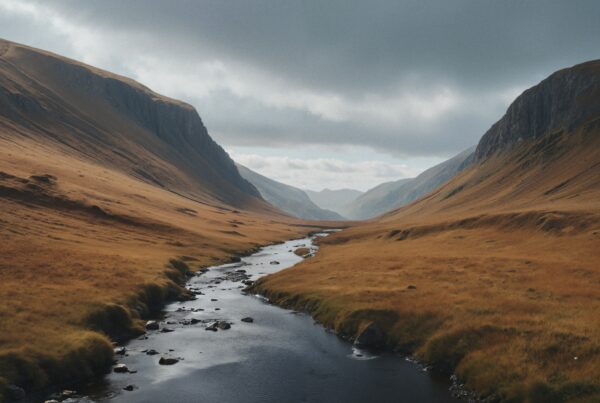 A tranquil river flows through a vast valley between towering mountains under a cloudy sky.