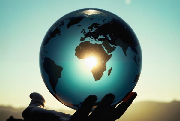 Silhouetted hand lifts globe at sunrise, symbolizing hope and interconnectedness.