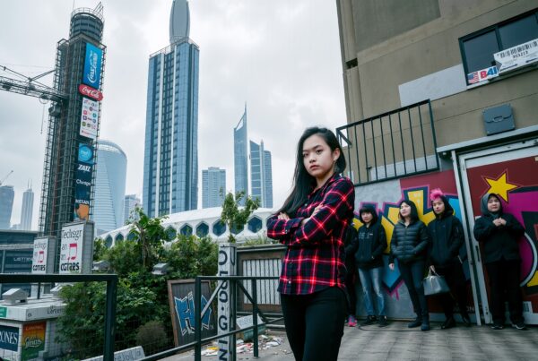 A young woman poses confidently against a backdrop of skyscrapers and graffiti in a vibrant urban setting.