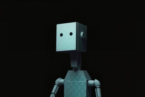 A minimalistic robot stands against a dark background, featuring a box-shaped head and metallic body.