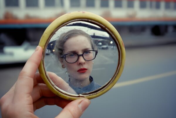 Person with red lipstick reflected in a handheld mirror by the road.