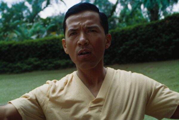 A man in a yellow shirt standing in a lush green park, displaying a focused expression amidst serene surroundings.