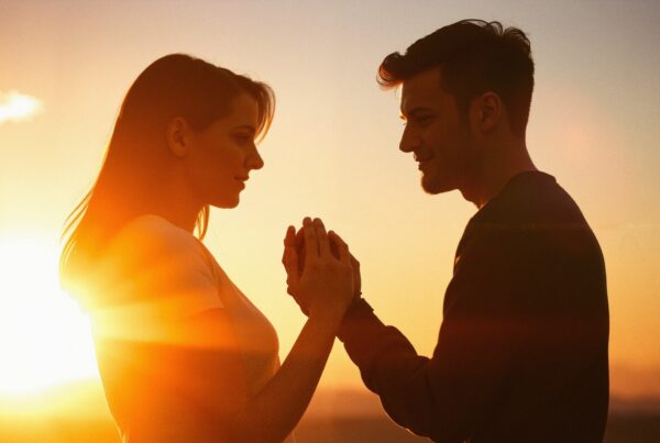 A couple holds hands at sunset, their silhouettes illuminated by the golden light, embodying romance and connection.