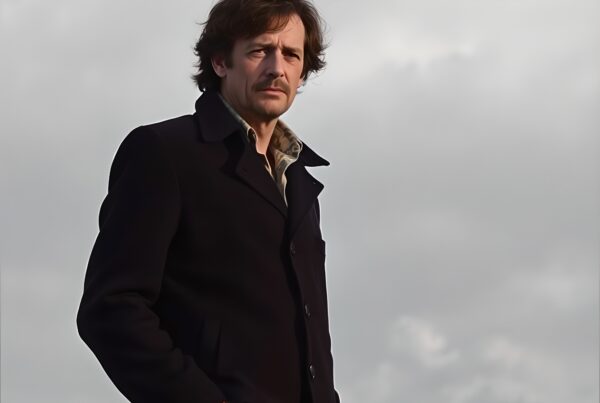 A man stands under a cloudy sky, hands in pockets, exuding a thoughtful demeanor.