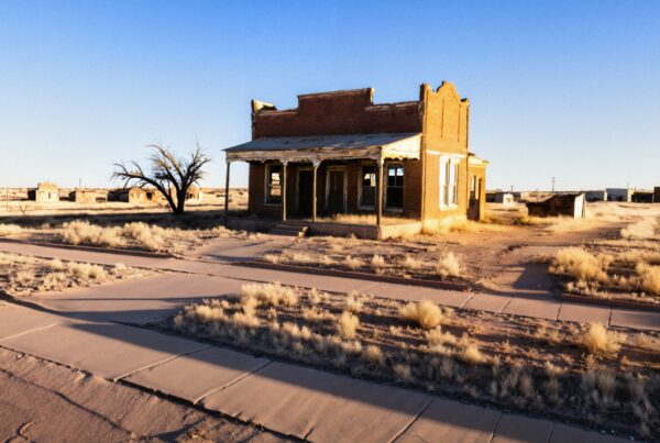 An abandoned brick building in a deserted landscape with dry grass and a clear blue sky.