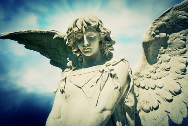 4K video loop of a serene stone angel statue with large wings against a bright blue time-lapse sky, illuminated by sunlight to create a divine and peaceful atmosphere.