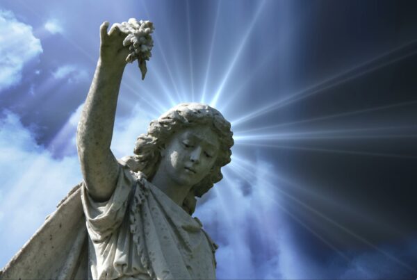 4K video loop of a serene stone angel statue with radiant light, holding flowers against a dramatic rime-lapse sky with beams and clouds.