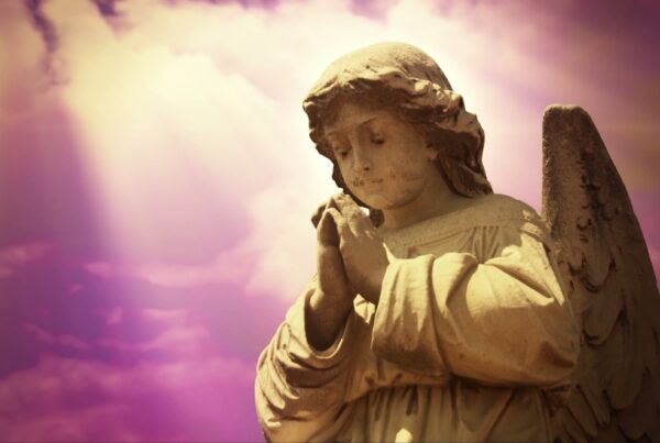 4K video loop of a serene angel statue with folded hands against a heavenly sky, bathed in warm light and surrounded by pink and purple time-lapse clouds.