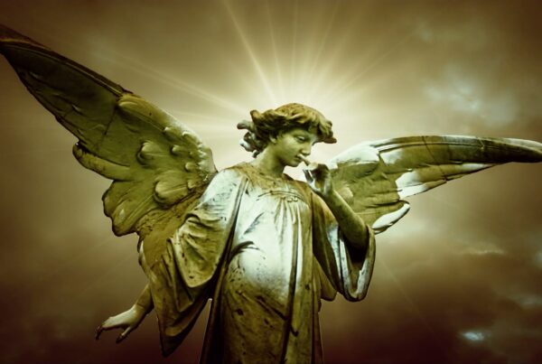 Stone angel statue with widespread wings set against a radiant, time-lapse cloudy sky, highlighting its serene expression and symbol of contemplation under diffused sunlight.