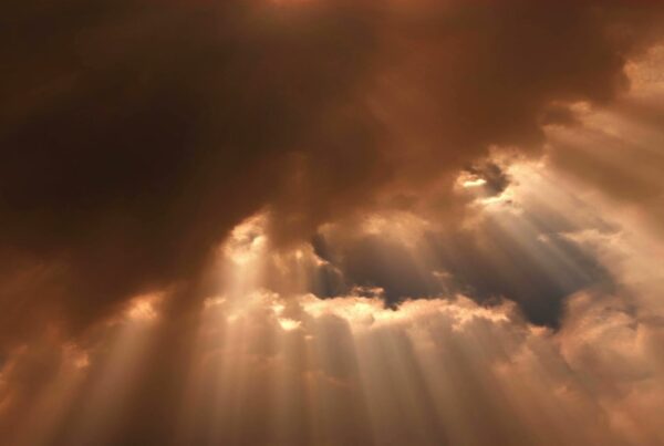 A sky dominated by dark, dense clouds with shafts of light piercing through the gaps in the clouds, video loop.