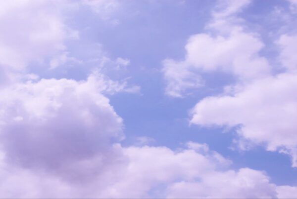 A serene sky scene featuring fluffy white time-lapse clouds with a soft purple hue set against a bright blue sky, creating a tranquil and peaceful atmosphere.