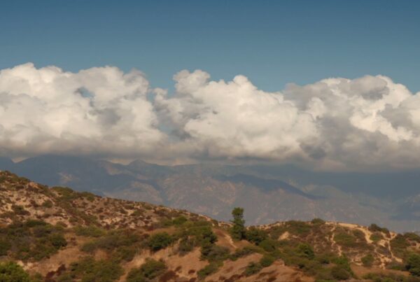 Majestic landscape with fluffy time-lapse clouds over rolling hills and distant mountains under a clear blue sky.
