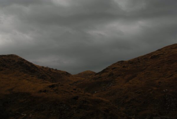4K video of rolling hills under a dramatic overcast sky with earthy tones and dark time-lapse clouds.