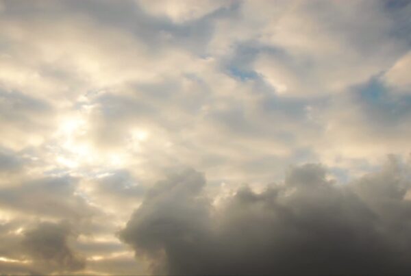 A dramatic evening sky filled with a mix of light and dark time-lapse clouds, with sunlight peeking through, creating a dynamic and serene atmosphere.