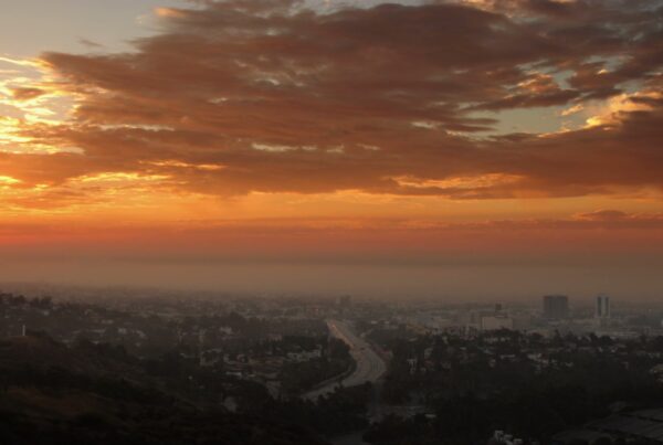 A breathtaking time-lapse sunset casts an golden orange glow over a sprawling cityscape, featuring silhouettes of buildings and a prominent road leading into the urban horizon, creating a serene and tranquil evening scene.