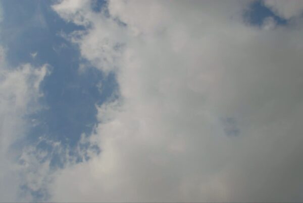 A scenic view of a time-lapse sky featuring a dramatic contrast between a clear blue area with wispy white clouds and dense greyish-white clouds, suggesting changing weather conditions.