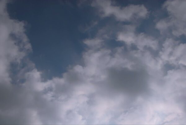 A tranquil sky with fluffy, wispy white time-lapse clouds spread across a rich blue background, creating a serene and peaceful atmosphere.