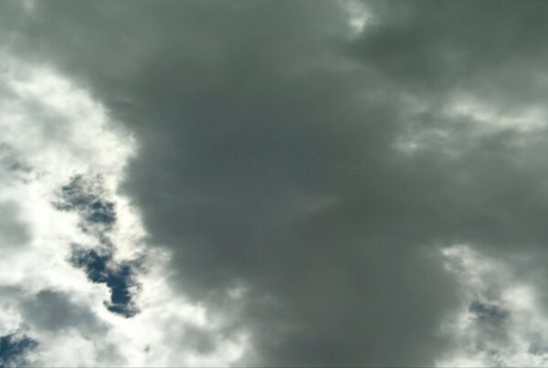 Dramatic time-lapse cloudy sky with dark, ominous clouds overshadowing the scene, contrasting with lighter patches and glimpses of blue sky, suggesting an upcoming storm.