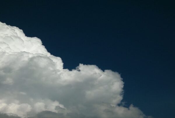 A large, white fluffy time-lapse cloud set against a deep blue sky, illuminated by sunlight, creating a peaceful and serene natural scene.