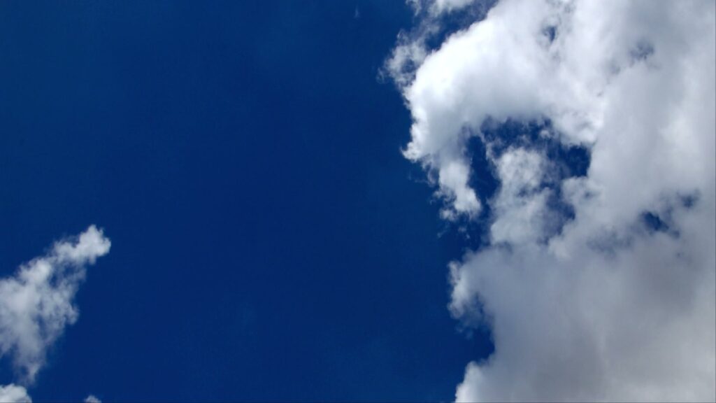 A vibrant blue sky partially covered by fluffy white time-lapse clouds, creating a serene and peaceful atmosphere.