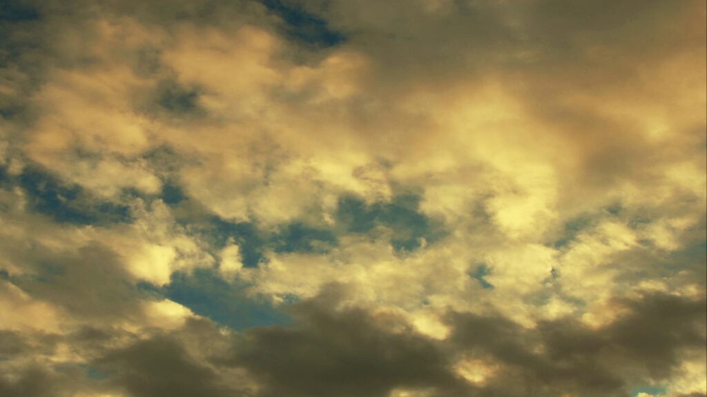 This video captures a beautiful sky filled with soft, fluffy time-lapse clouds in light cream and golden hues.