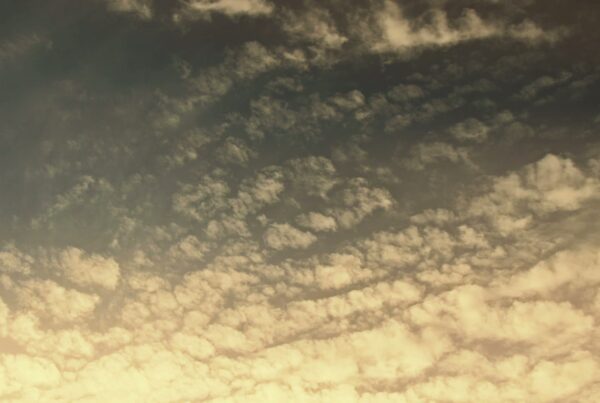 A peaceful sky filled with scattered, fluffy time-lapse clouds transitioning from a golden hue at the bottom to a darker shade above, creating a serene atmosphere during sunrise or sunset.