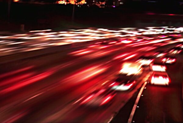 A looping video of a dynamic nighttime highway scene with long exposure captures colorful light trails from fast-moving cars, set against a backdrop of city lights.