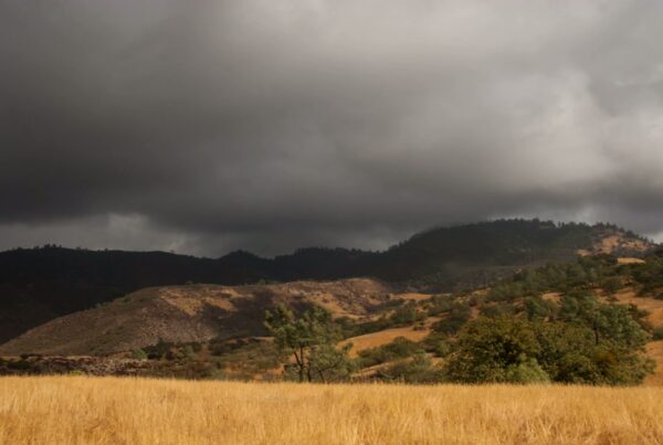 Dark time-lapse storm clouds travel over rural hills and a grassy field landscape.
