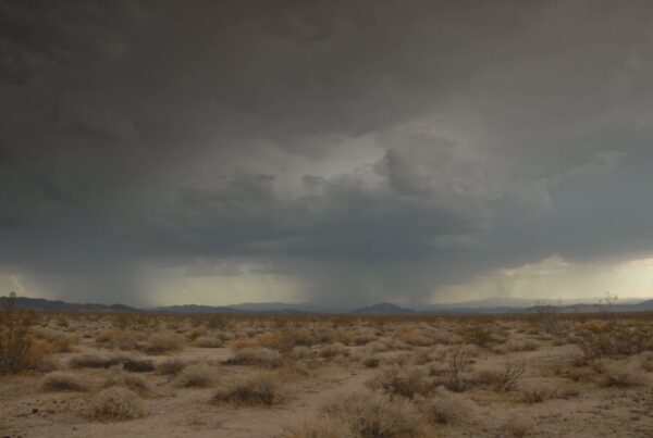 The video captures a vast desert landscape under the looming presence of dark storm clouds and lightning.