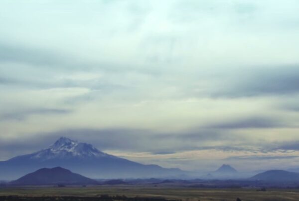 Majestic snow-capped mountain landscape with time-lapse cloudy skies, featuring expansive plains and distant hills under a serene and peaceful atmosphere.