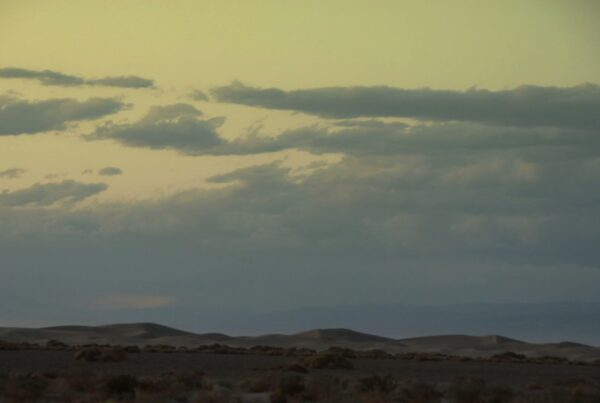 A serene desert landscape with rolling dunes under a time-lapse cloudy sky at dawn or dusk, showcasing natural beauty and tranquility.