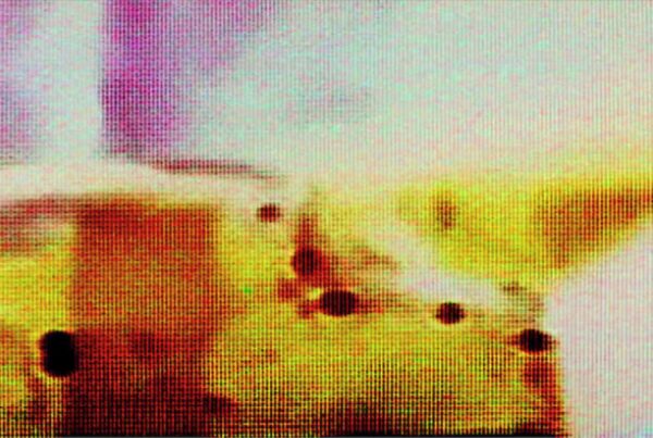 A vivid abstract video loop composed of colorful pixelation featuring dominant yellows and purples with contrasting dark spots scattered across the screen.