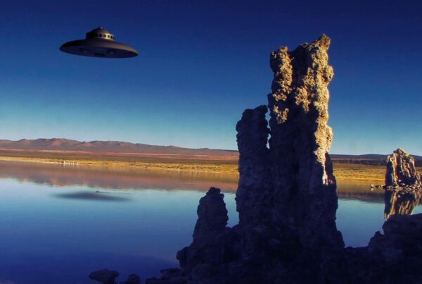 HD video of an alien spacecraft hovering over a serene lake with rocky formations in a scenic landscape.