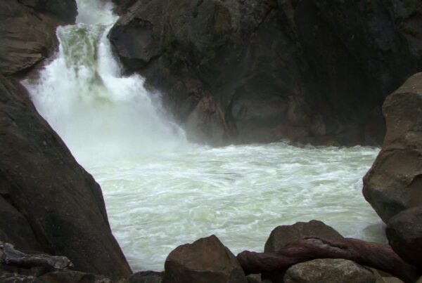 Powerful waterfall cascading over rugged rocks surrounded by a natural wilderness, with mist rising from the frothy water below.