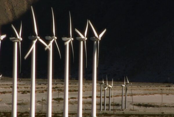 Wind turbines in a desert landscape against a mountain backdrop, highlighting clean energy and sustainable technology in an arid environment.