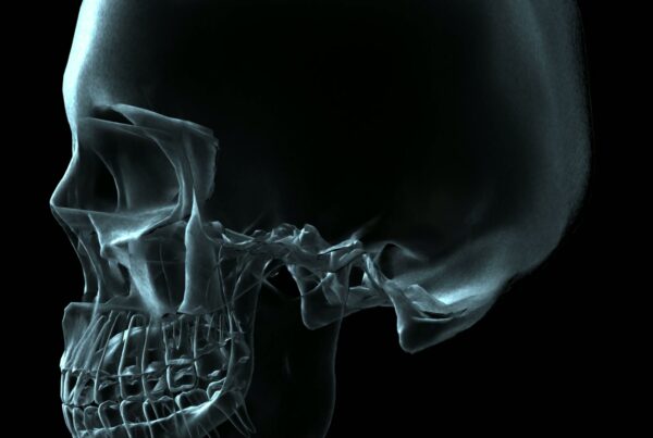 A video loop of a rotating human skull in X-ray style against a dark background, highlighting intricate bone details.