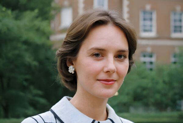 Portrait of a woman with short brown hair, wearing a white top, in front of a brick building.