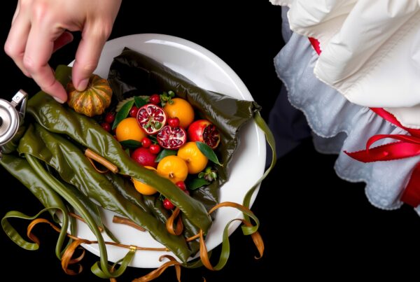 Vibrant fruits with green leaves and teapot on a white plate.