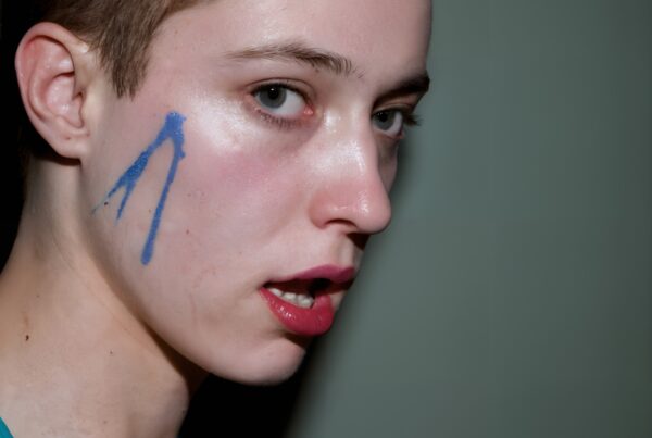 Person with blue face paint, expressing creative emotion in minimalist portrait.
