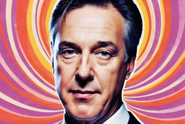 A man in a suit stands against a vibrant swirl background.