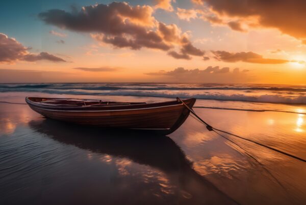 A wooden boat rests on a tranquil beach during a striking orange sunset with the ocean waves gently rolling in.