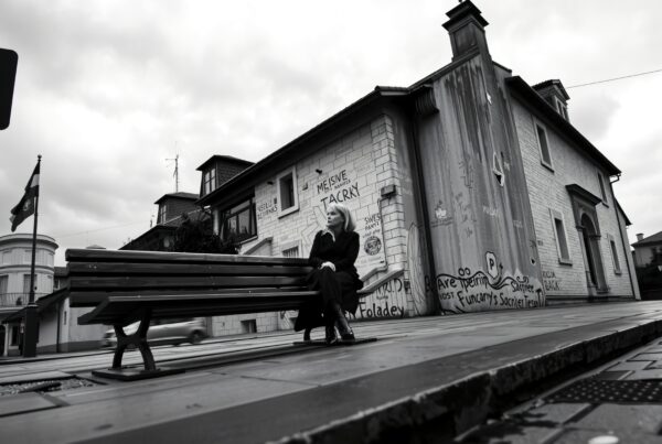 A person sits on a bench beside a graffiti-covered building in an urban black and white street scene.