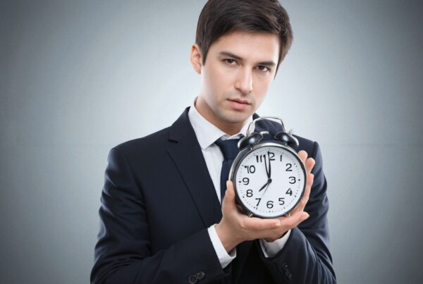 A man in a suit holding a large alarm clock, conveying urgency and time management.