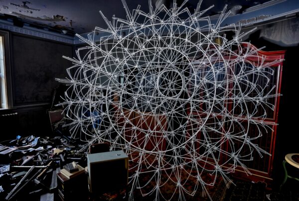 A complex geometric sculpture inside a cluttered room featuring white intersecting lines.