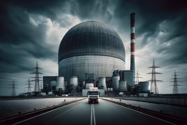 A large truck approaches a nuclear power plant under a stormy sky, highlighting the facility's massive industrial architecture.