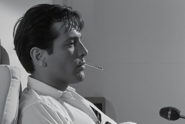 Young man with cigarette in profile, microphone nearby, monochrome image.