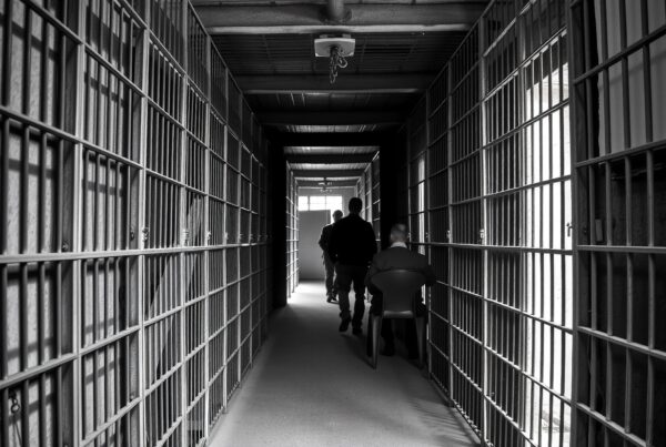 Black and white prison hallway with two figures walking.