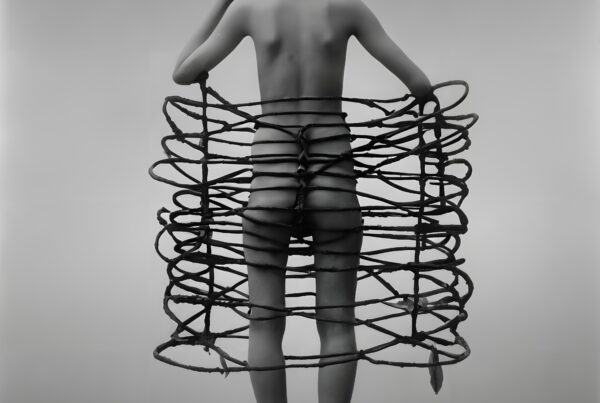 Artistic nude photography with a conceptual twist, featuring a person enveloped in a spiraling, branch-like cage structure against a minimalist background.