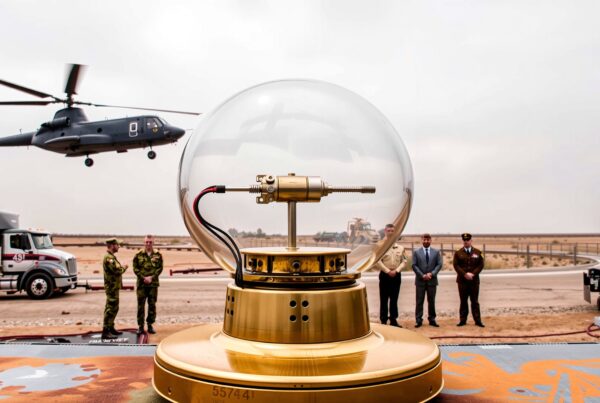 A helicopter hovers above a high-tech device in a desert setting.